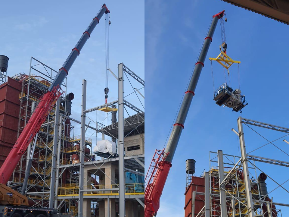 Guindaste de grande porte realizando o içamento de um gerador industrial utilizando balancim de carga para posicionamento em estrutura metálica de galpão.