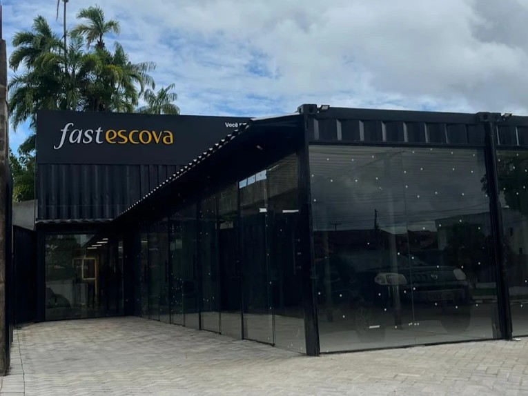 Fachada moderna da Fast Escova construída em containers pretos com grandes vitrines de vidro temperado e letreiro iluminado sob céu nublado.