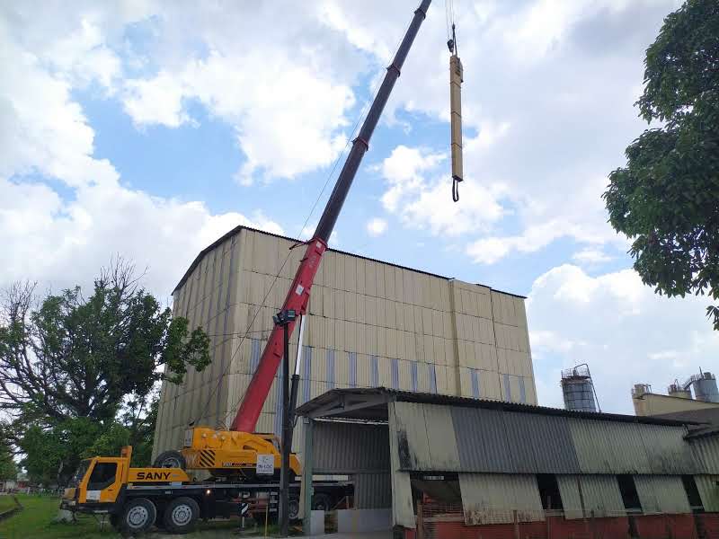 Guindaste Sany vermelho e amarelo com lança telescópica estendida em ângulo vertical para içamento de carga no topo de um galpão industrial em Barcarena.