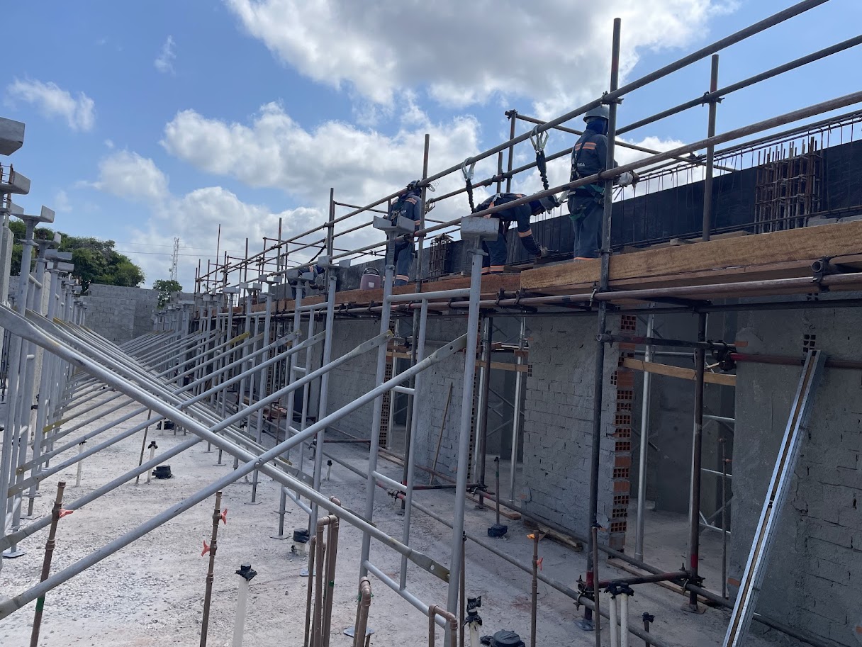 Operários em plataforma de andaime tubular fachadeiro realizando concretagem de viga sobre parede de blocos de concreto em canteiro de obras em Moju.