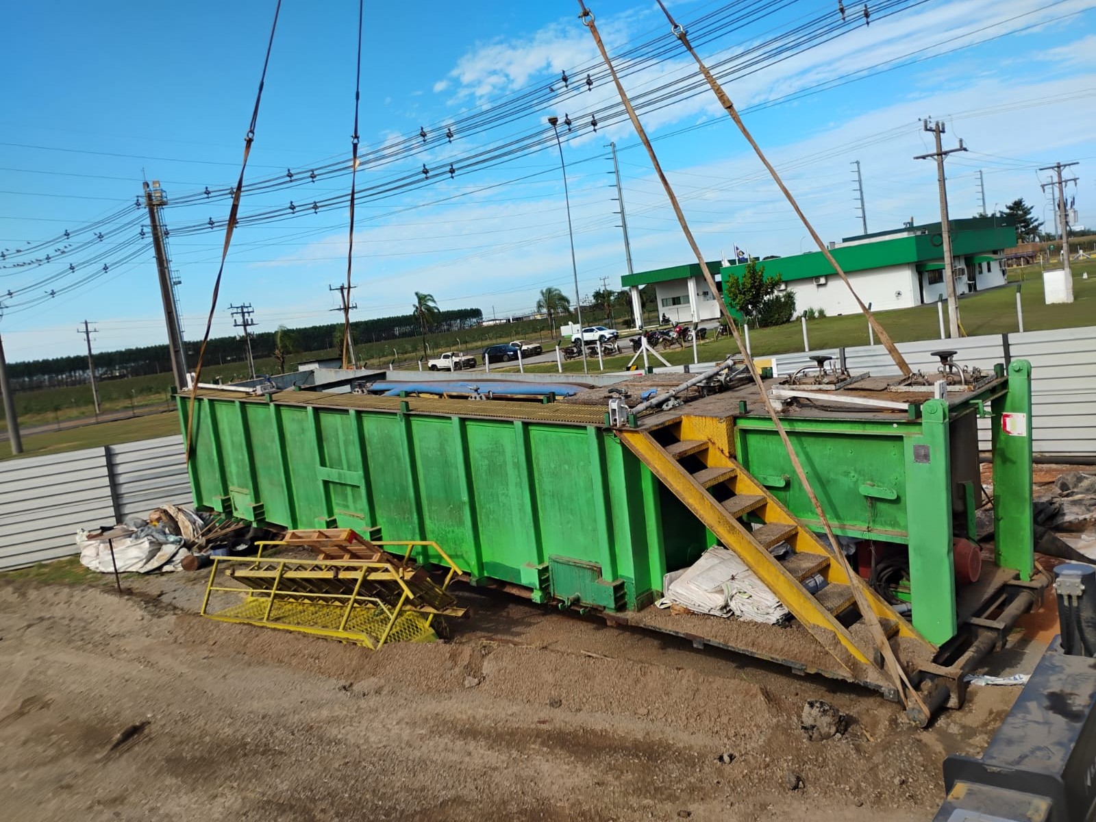 Içamento de módulo habitável ou container tanque verde com escada de madeira acoplada, sendo movimentado por cabos de aço em canteiro de obras em MATO GROSSO
