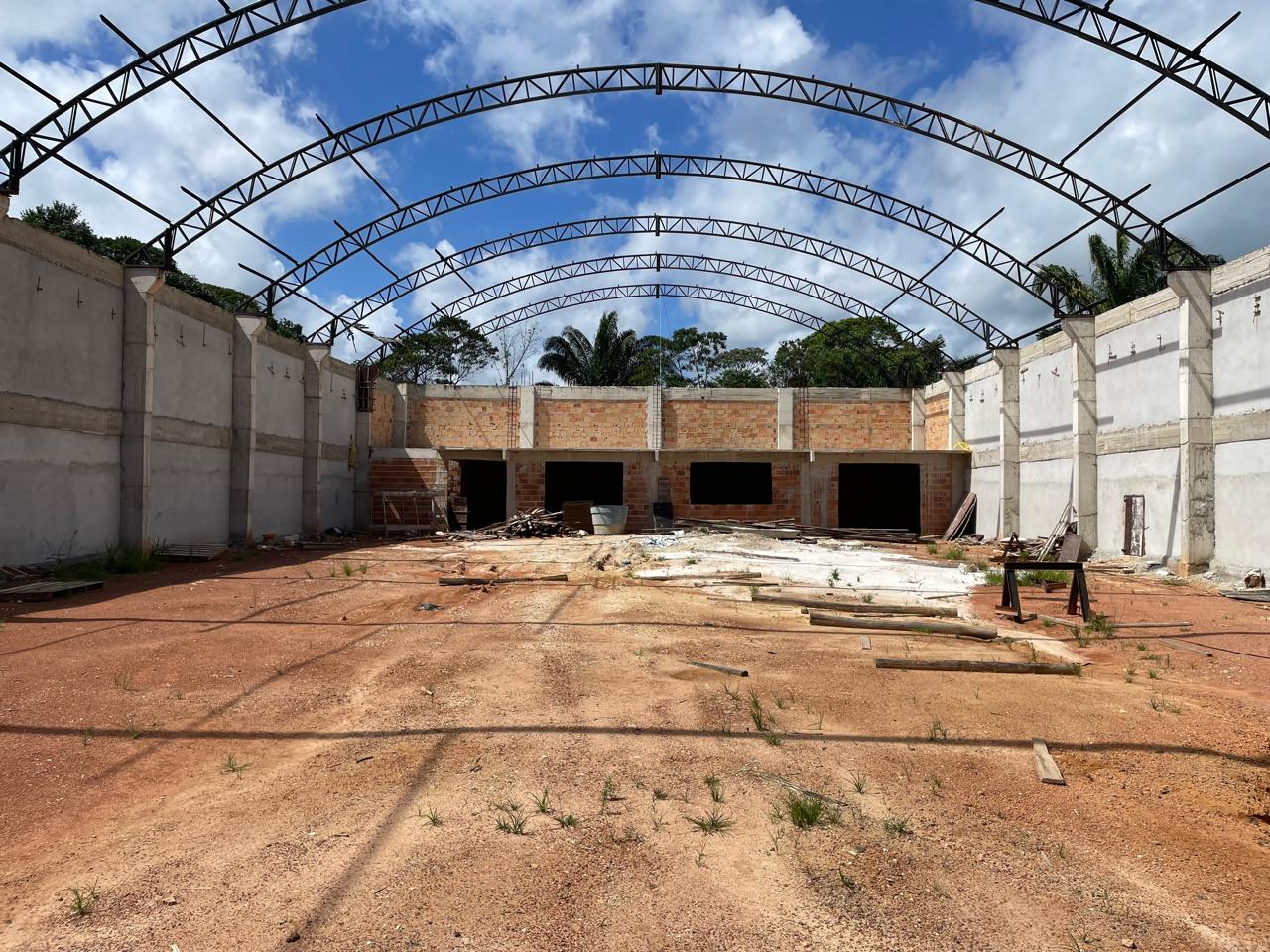 Vista interna de grande galpão comercial em construção em Barcarena, mostrando pilares de concreto, área de dois pavimentos ao fundo e estrutura de arcos metálicos para o telhado.