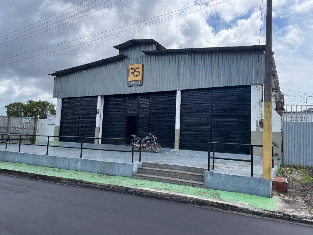 Fachada do galpão comercial Brasil Mar em Barcarena, com estrutura metálica cinza, três grandes portões de enrolar pretos e rampa de acesso frontal sob céu nublado.