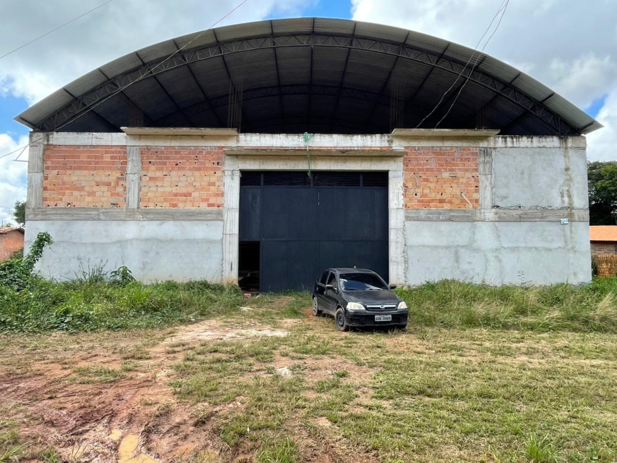 Vista frontal de galpão comercial em construção com estrutura mista de concreto e aço, apresentando grande portão metálico preto e cobertura em arco.