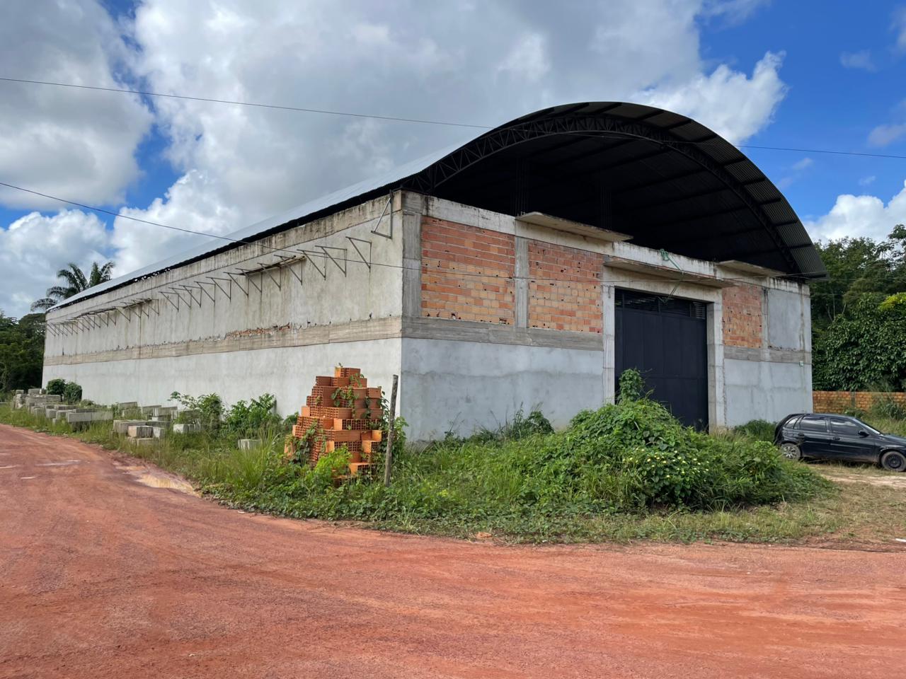 Vista externa de galpão comercial de grande porte em construção com paredes de tijolo aparente, vigas de concreto armado e cobertura metálica em arco em Barcarena.