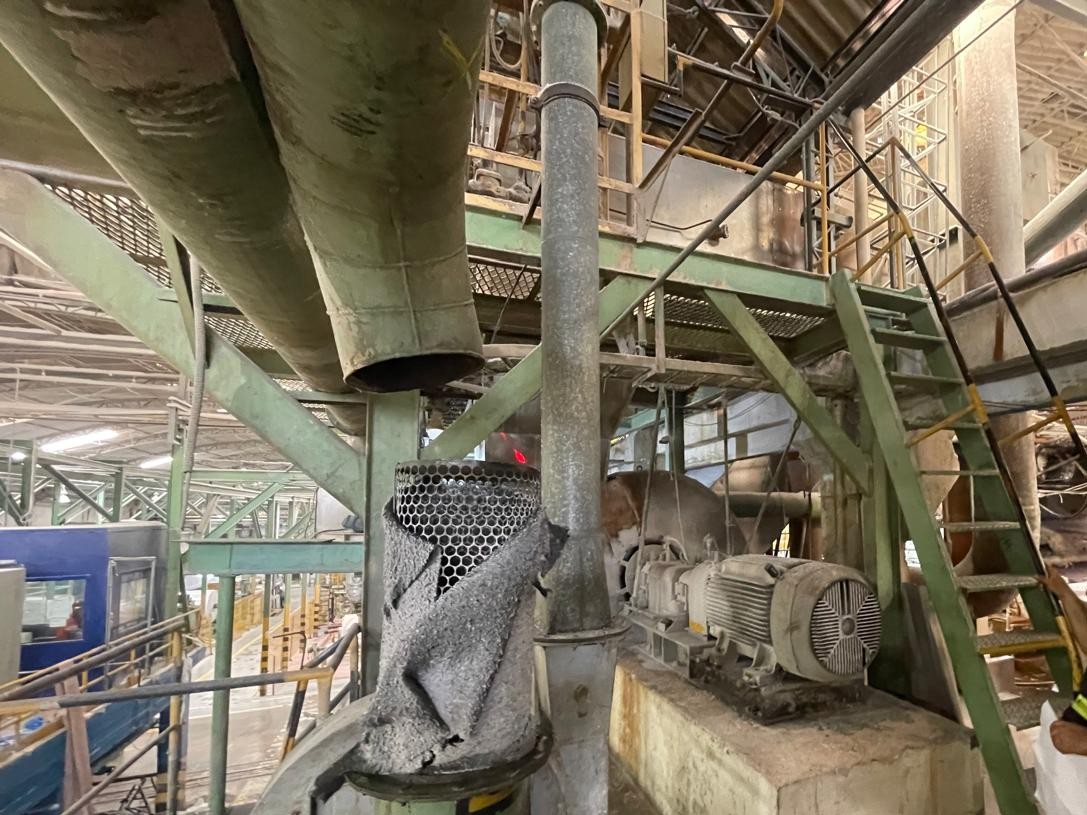 Vista interna de uma planta industrial com tubulações de grande diâmetro, motores elétricos, escadas metálicas de acesso e estruturas de suporte em aço.