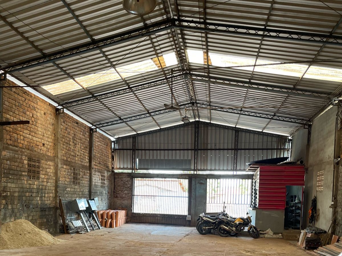 Vista interna do galpão da Metal Lima com pé-direito alto, estrutura de telhado metálico com telhas translúcidas para iluminação natural e paredes de alvenaria.