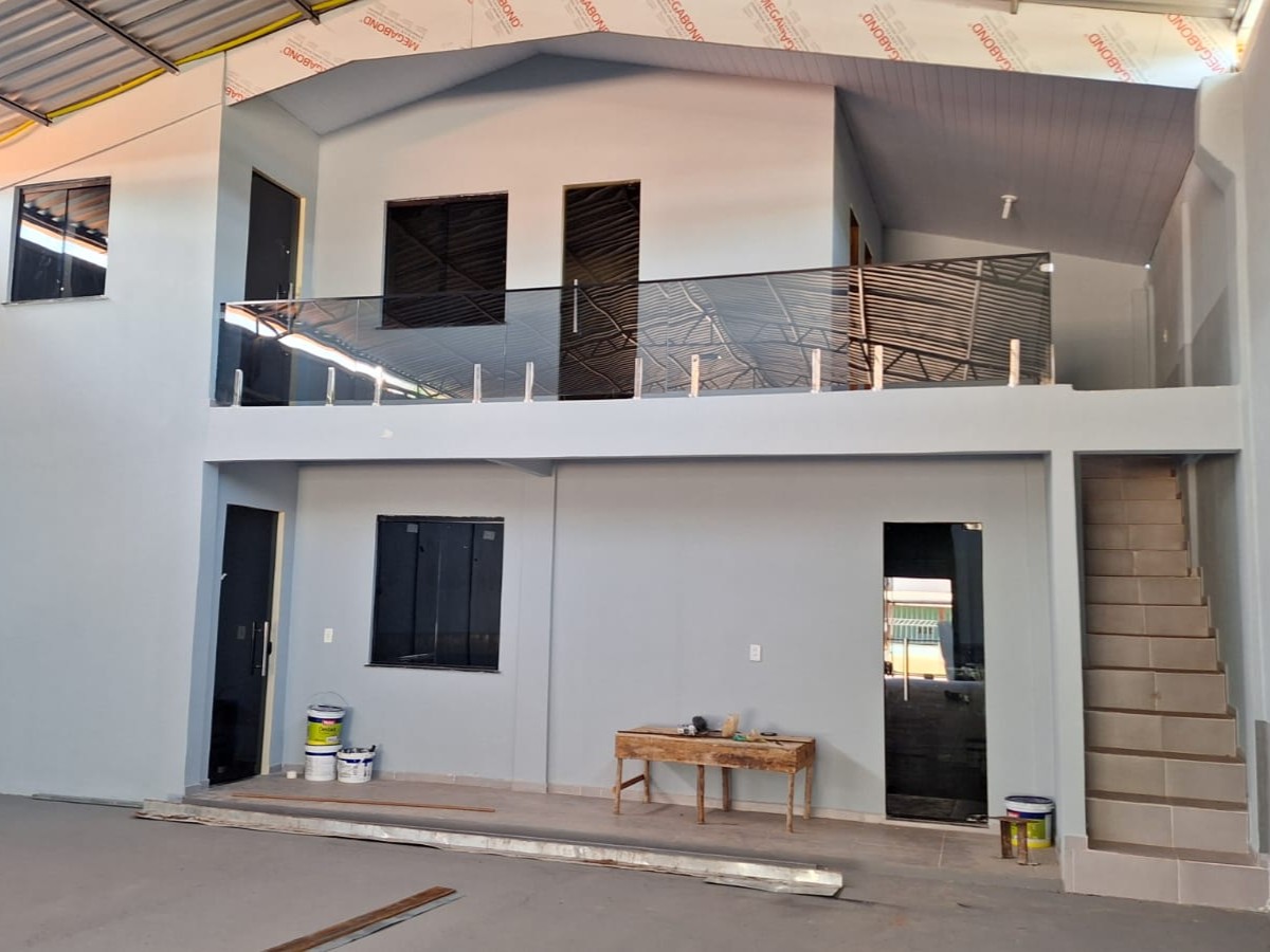 Vista interna de galpão comercial em Barcarena com estrutura de dois pavimentos em fase de acabamento, destacando guarda-corpo de vidro fumê, escada lateral e pintura cinza.