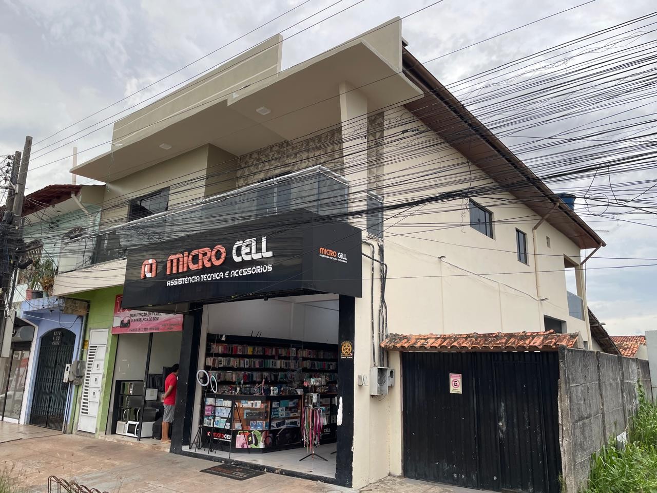 Fachada moderna da loja Micro Cell em Barcarena, apresentando testeira em ACM preto com letreiro branco iluminado, vitrine ampla e estrutura predial revitalizada.