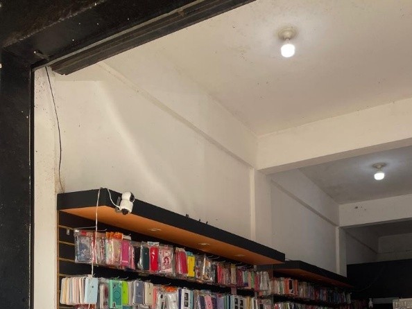 Vista interna de loja comercial com prateleiras de acessórios de celular, destacando o forro de gesso com sancas e fiação elétrica de câmera de segurança aparente na parede.