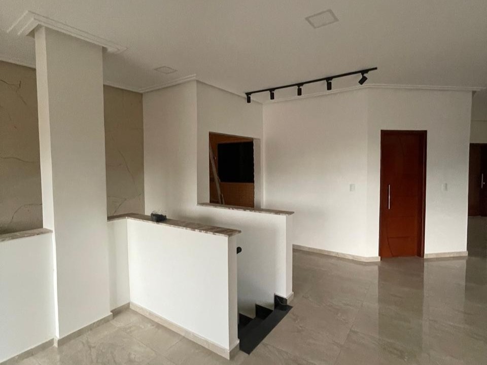 Interior de imóvel reformado com piso em porcelanato polido, escada com granito escuro, paredes brancas, sanca de gesso e trilho de iluminação spot preto.