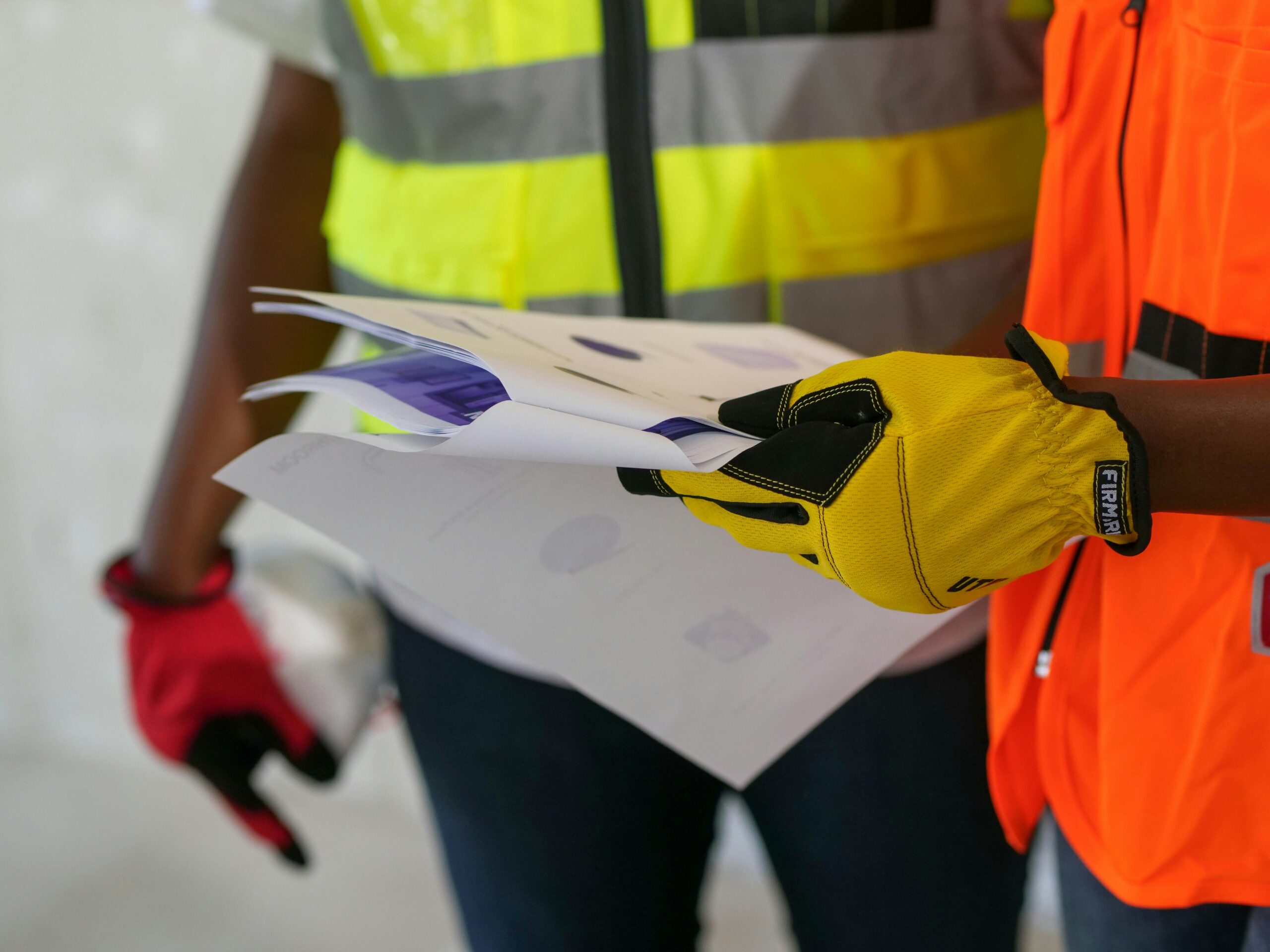 Artigos Close-up of construction workers reviewing documents wearing protective gear. Safety-focused interaction.